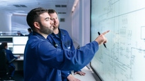 Two IT experts, like developer, data engineer or IT consultant, standing in front of a big display at the BASF location Ludwigshafen.