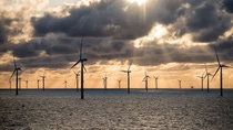 Wind park "Oersted" in the German North sea at sunset, large grey clouds shield the sun in an orange sky.