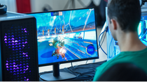 Person sitzt an einem Desktop-PC und spielt ein schnelles Videospiel auf einem Monitor; daneben steht ein beleuchteter Gaming-PC mit sichtbaren LED-Komponenten. Person sitzt an einem Desktop-PC und spielt ein schnelles Videospiel auf einem Monitor; daneben steht ein beleuchteter Gaming-PC mit sichtbaren LED-Komponenten.
