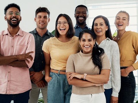A group of young talents stand in a bright office room and smile at the camera.